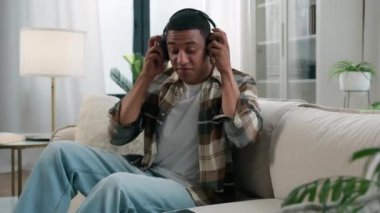 Afro-Amerikalı bir adam oturma odasına gelip evdeki kanepeye oturur ve kablosuz kulaklık takar. Cep telefonuyla müzik dinler. Kulaklıkla müzik dinler.