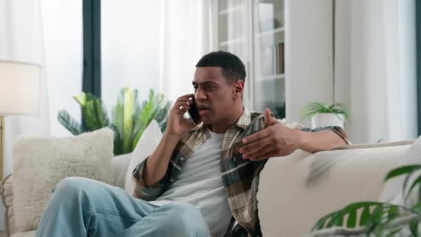 非洲裔美国人愤怒的争论对方在电话争论冲突智能手机对话问题讲手机不快乐的男人在家里沙发上生气的男人讲手机紧张的争吵 — 图库视频影像