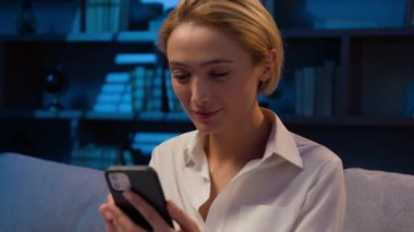Akşamları beyaz bir kadın cep telefonuyla sosyal medyada geziniyor. İnternetten internet alışverişi yapıyor. Akıllı telefonlu iş kadını kameraya gülümsüyor.