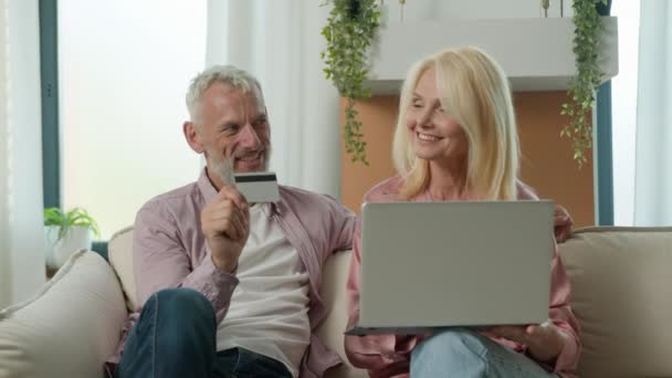 幸せな高齢者コーカサス家族カップル男性祖父母リモート有料年金クレジットカードをインターネットで自宅でラップトップを使用して家で購入するオンラインストアで支払う電子銀行サービスの安全な支払 — ストック動画
