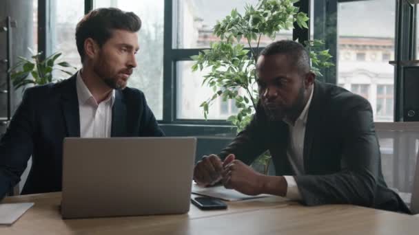 アフリカ系アメリカ人のビジネスマンは 白人の貿易業者の代理人が銀行の書類のデータをチェックするのを聞く ラップトップオンラインプロジェクトスタートアップビジネスディスカッションを持つ2つの多様な多人種間のビジネスマン — ストック動画