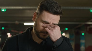 Hüzünlü iş adamını kapat. Yorgun, Kafkasyalı, sinirli, gözleri ovuşturan, göz yorgunluğu çeken, ağlayan, keder gözyaşı döken, karanlık otoparkta görme bozukluğu, baş ağrısı, göz doktoru.