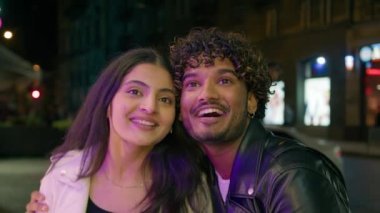Arap Hindistanlı mutlu bir çift, şehirde aşık, sokak geceleriyle flört ediyor, vitrine bakıyor, gülüyor, indirimli konuşuyor, hediyeler seçiyor, dijital ekran yansıtma sinemasına bakıyor.