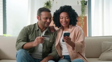 Mutlu Afrikalı Amerikalı evli çift karı koca, internet sitesine kredi kartıyla ödeme yapıyor. Cep telefonuyla, çok ırklı ailelerin gülümsediği müşteriler ev telefonlarıyla kolay para ödüyor.