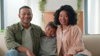 Çok ırklı Afro-Amerikan beyaz mutlu aile portresi evde gülümseyen ebeveynler baba ve anne küçük çocuğa sarılıyor kanepe kanepesinde çocuk anaokulu çocuğu çeşitli nesiller çocukları seviyor.