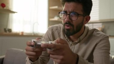 Bağımlı erkek oyuncu Arap adam kanepede video oyunu oynuyor uzaktan kumandalı kumanda kumandalı kumanda, sanal oyun bağımlılığı mutfakta TV ev eğlencelerinde konsol oyunu oynuyor.