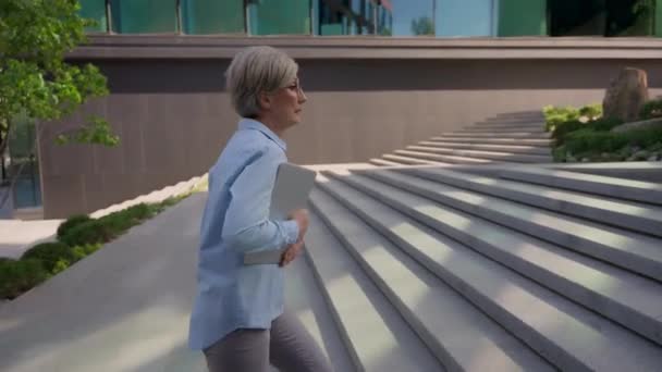 コーカサス州の成熟したビジネス女性は フォルダの遅延時間で動作するために速く実行している忙しいシニアのビジネス女性の雇用主を見て 市内の階段オフィスビルを歩いています — ストック動画