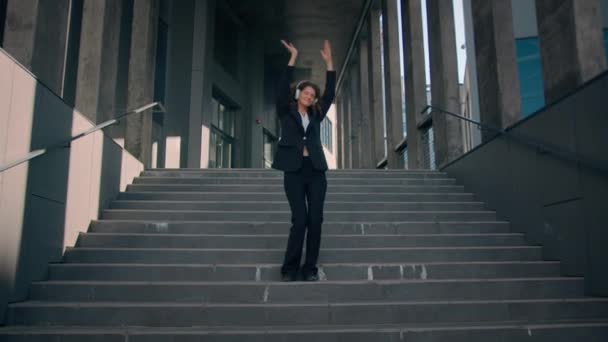 踊る楽しい幸せな面白いコーカサス女の子のビジネスマンは音楽ヘッドフォンを聞くオフィスの建物の外の階段を歩く歌を楽しんでプロのビジネス女性ダンス都市の自由なライフスタイル — ストック動画