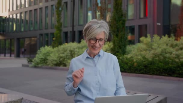 成熟した灰色の髪の女性コーカサス女性シニア女性グリーティングクライアントオンライン話すラップトップデバイスビジネスコミュニケーション笑顔の幸せな中年のビジネスウーマン屋外でのコール — ストック動画