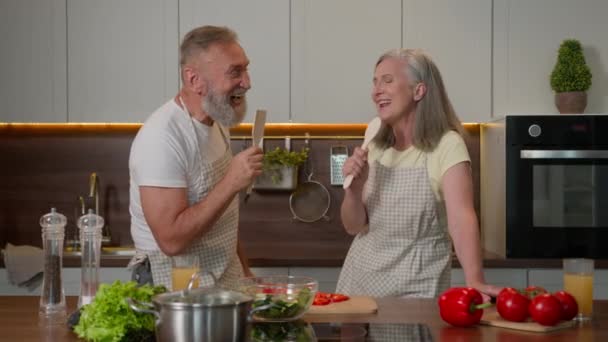 有趣的白种人夫妇恋爱中成熟的中年妇女和丈夫退休的已婚家庭在勺子里唱歌厨房里快乐的笑着的女人男人在厨房里快乐地做饭健康的食物 — 图库视频影像