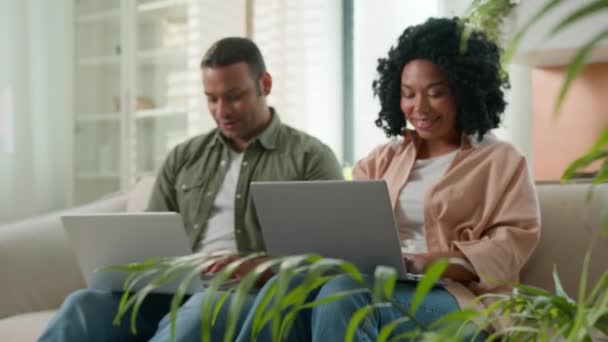 恋爱中的多种族夫妇在家里的笔记本电脑上工作非洲裔美国人的家庭生意人们一起在网上沙发上购物 在电脑上看着镜头微笑的男女使用设备 — 图库视频影像