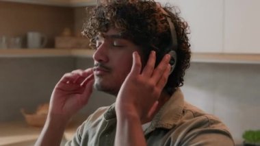 Mutlu İspanyol erkek Hintli Arap adam modern kablosuz kulaklıklarla müzik dinlerken gülümsüyor kulaklıkla dans ediyor hafta sonu ev mutfağında ses dansının tadını çıkarıyor ritim tutmak için parmaklarını şaklatıyor.