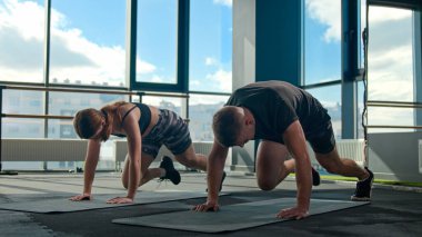 Beyaz tenli sporcu erkek sporcu kadın sporcu vücut geliştiriciler dağcı egzersizleri yapıyor spor salonunda kas gevşetici bacakları kaldırıyor spor salonunda enerji kaybı kardiyo egzersizi yapıyor.