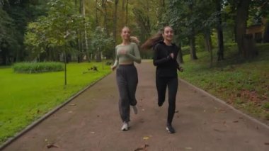Kafkasyalı genç bayan koşucular koşucular sporcu bayan arkadaşlar parkta birlikte koşuyorlar gülümsüyorlar iki sağlıklı kadın koşuyor sağlıklı yaşam tarzının keyfini çıkarıyorlar sabah koşusu dışarıda sabah aktivitesi