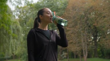 Şehir parkında antrenman yaptıktan sonra spor yapan beyaz kadın. Şişe temiz su. Kadın sporcu. Sağlıklı beslenme, kilo kaybı.