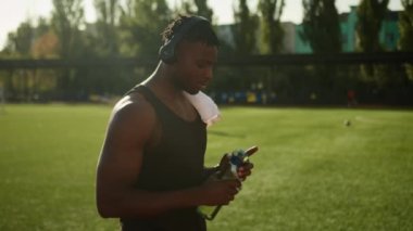 Fitness sporcusu spor şişesinden su içiyor şehir ferahlatıcısı hidratsız vücut egzersizi dinleniyor yorgun Afrikalı Amerikalı adam kulaklıkla müzik dinliyor.