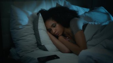 Güzel Afro-Amerikalı kız yatağında uyuyor. Uyandı. Çalar saati kapattı. Cep telefonu mesajı tetikledi.
