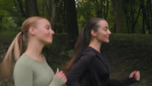 快乐的女性跑步者两个白人女孩在公园里慢跑 笑着活跃的女性享受着有氧运动健康的生活方式早晨的活动在城市的室外慢跑锻炼 — 图库视频影像