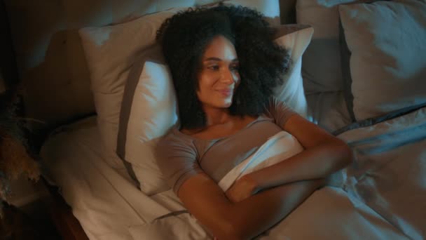 平和なリラックスしたアフリカ系アメリカ人女性 ダークベッドルームの夜に横たわる美しい女の子 休憩甘い夢のベッドタイムレクリエーション 笑顔の女性 居心地の良いベッドでリラックス 整形外科枕マットレス — ストック動画
