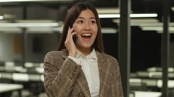 Amazed wonder surprised Asian girl student indoors listening good news mobile phone call excited happy Korean business woman Japanese businesswoman Chinese female in office talk smartphone achieve