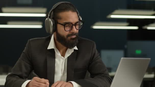 インドの男性はヘッドセットのアラビアのビジネスマンをヘッドホン起業家で身に着けています ノートブックレビュービジネス教育 オフィスでラップトップコンピュータを勉強する カメラで笑顔 — ストック動画