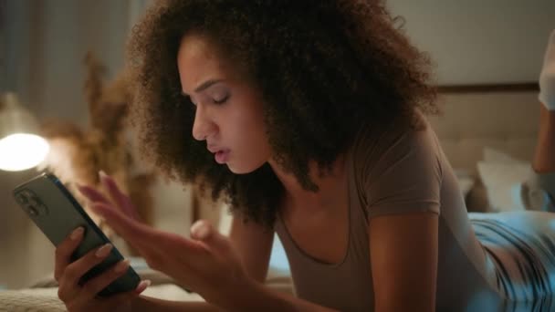 携帯電話デバイスを見ている悲しいアフリカ系アメリカ人女性は スマートフォンでベッドに横たわるイライラした民族の女性Zの少女が夜の自宅で詐欺メッセージの損失エラーを心配しました — ストック動画