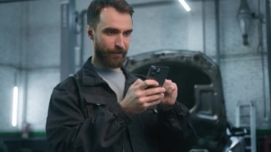 Otomobil tamircisi, beyaz erkek, yönetici, bakım mühendisi. Cep telefonu ekranına bakıyor. Neşeli, gülen akıllı telefon.