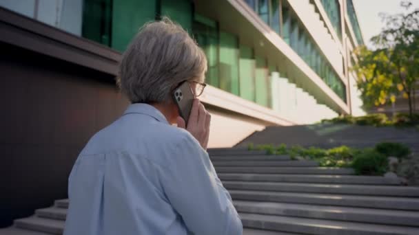 バックビュー 白人女性 成熟した ビジネスウーマン 雇用主 街の階段を歩く 未知のビジネス 携帯電話 コミュニケーション 屋外で話す — ストック動画