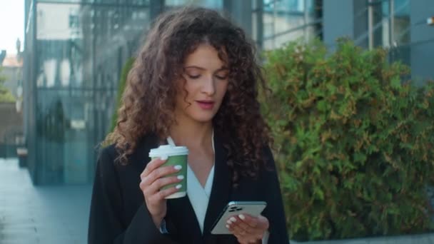 白人夢見る少女ビジネス女性 スマートフォンでスマートフォンチャットメッセージを使用して街角を歩く オンライン注文 思慮深いビジネスマンは外でコーヒー朝の仕事のカップを保持します — ストック動画