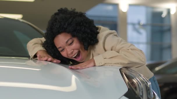 幸せな女性 アフリカ系アメリカ人女性の女性のバイヤーのクライアントは 新しいモダンな車の喜び笑顔の女の子のフードを抱擁店のサロンディーラーで豪華な自動車にリーク車で車を購入夢見ています — ストック動画