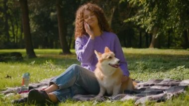 Mutlu beyaz kadın, genç, güzel, 20 'li yaşlarda kız arkadaşıyla parkta cep telefonu konuşuyor. Bu arada küçük köpek, haftasonu çimenlerde oynayan Welsh Corgi, dışarıda köpek yavrusuyla dinleniyor.