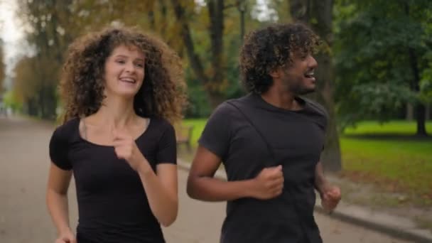 两名多种族运动员快乐的阿拉伯印第安人男子白人女子在城市公园里跑步 一起积极参加晨练 挥手打招呼 摆出友好的女性男子在户外慢跑的姿势 — 图库视频影像