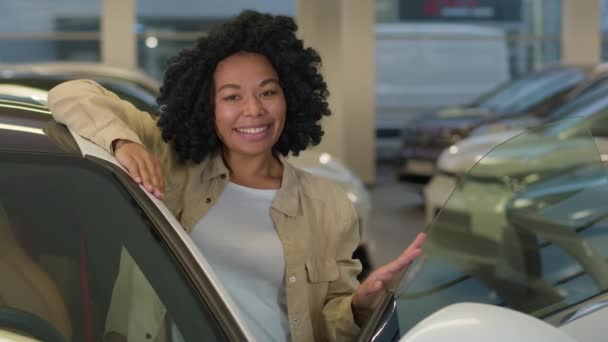 アフリカ系アメリカ人の女の子の顧客バイヤーの顧客ドライバーは 自動車ショールームで新しい電気自動車を購入します 車両サロンディーラー店で車販売リースを笑う幸せな陽気なビジネス女性の肖像画 — ストック動画
