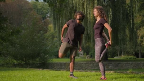 两名朋友体育夫妇运动员印度男子白种人女子公园自然训练男运动员女运动员一起伸展腿与个人健身教练在室外锻炼 — 图库视频影像