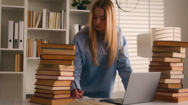 Kafkasyalı liseli kız öğrenci Kafkasyalı genç kız öğrencinin ev üniversite kütüphanesinde öğrenme sınavına hazırlanırken dizüstü bilgisayar kullanarak birçok kitap yazmakla meşgul.