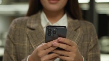 Gülümseyen Asyalı kız öğrenci Koreli mutlu iş kadını Japon iş kadını ofis şirketindeki Çinli kadın Malezyalı girişimci yönetici işveren cep telefonu gülümsemesi kullanarak kameraya bakıyor.