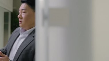 Yorgun Asyalı işadamı üzgün Koreli Çinli bir Japon 'u üzdü ofis koridorunda duvara yaslanmış hayal kırıklığına uğramış orta yaşlı, akıllı telefonlu bir erkek kötü haber sorunları okudu.