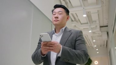 Düşünceli Asyalı yetişkin 40 'lı yaşlarda kıdemli işadamı akıllı telefon uygulamasına göz gezdiriyor internet üzerinden iş bağlantıları kuruyor Çinli Koreli Japon erkek işveren patronuyla telefon interneti kullanıyor.