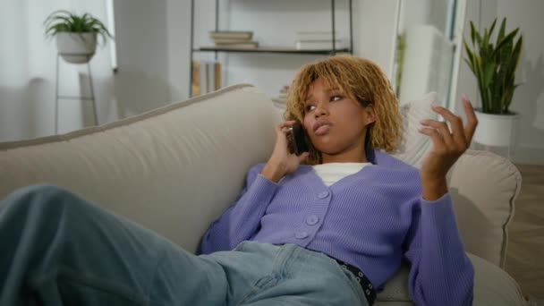 アフリカ系アメリカ人の悲しい落ち着いた静かな静かな落ち着いた女性のソファーでリラックスしたリビングルームで女性の民族的な女性 スマートフォン通話で携帯電話注文の食品配達 — ストック動画