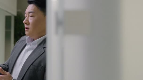 疲れ切ったアジアのビジネスマンは オフィスで壁に傾いている悲しい大人の韓国人中国人日本人の男性は スマートフォン携帯電話で欲求不満中年男性を読んで悪いニュースビジネス問題 — ストック動画