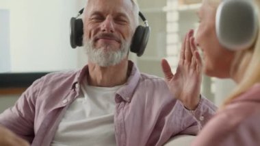 Mutlu kaygısız Kafkasyalı çift kadın 60 'lı yaşlardaki büyükanne büyükbaba emekliler kulaklıkla müzik dinliyorlar evde dans ediyorlar kulaklıklarda müzik sesleri dinliyorlar şarkıların tadını çıkarıyorlar