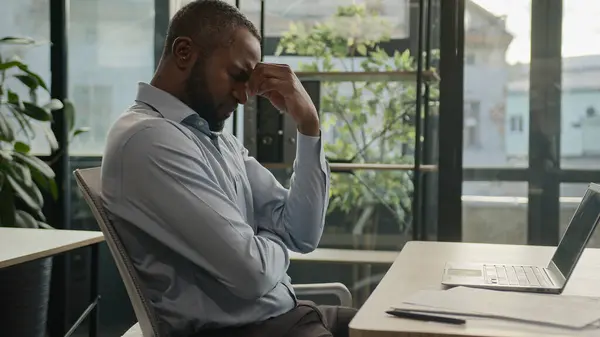 Exhausted sick mature senior businessman tired African American ethnic man office executive work on computer typing feel headache pain eyestrain fatigue health problem suffer migraine ache sit indoors