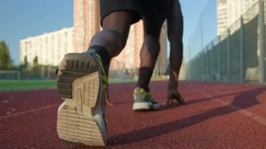 Düşük pozisyonlu arka görüş koşucusu Afrikalı Amerikalı erkek sporcu koşuya hazırlanıyor erkek koşucu maraton koşuyor aktif spor eğitimi alıyor şehir güneşinde koşuyor.