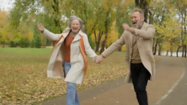 Sonbahar parkında eğlenen komik romantik yaşlı çift olgun kadın ve erkek mutlu aile birlikte dans ediyor el ele tutuşuyorlar mutluluktan zıplıyorlar şehirde aktif emeklilik dansı yapıyorlar.