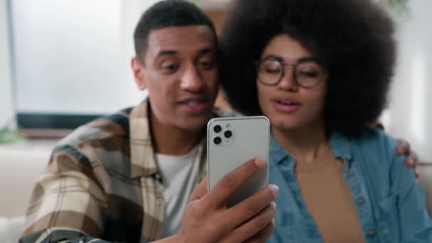 ハッピー笑顔のアフリカ系アメリカ人のカップリング抱擁民族の家族の男性の女性カップルは 家庭で話すカメラ会議でバーチャル会議ビデオ通話を持っている友人の両親に話す携帯電話を持っています — ストック動画