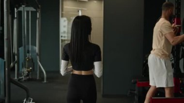 Kafkasyalı bir kadının, spor salonundaki antrenmandan sonra duşa girerken, halterci bir sporcuyla egzersiz yapan Afrikalı Amerikalı bir adamı selamlamasını. Spor salonunda beşlik çakın.