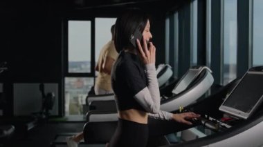 Spor salonundaki beyaz kadın sporcu kız cep telefonuyla konuşuyor sporcu kadın sporcu kadın koşu bandı kardiyo egzersizinde akıllı telefonla konuşuyor. Spor salonunda çok ırklı insanlar antrenman yapıyor.