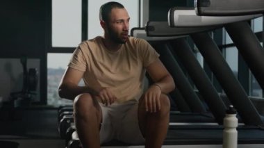 Atletik adam yorgun Afrika kökenli Amerikalı susamış erkek sporcu sporcu su içiyor fitness şişesi içme alışkanlığından protein içiyor spor salonunda dinleniyor koşu bandında kardiyo egzersizi yapıyor.
