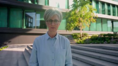 Kendine güvenen, 60 'lı yaşlarda, beyaz, orta yaşlı, gözlüklü bir iş kadını. CEO' su. Yönetici. Şehir merkezindeki kadın iş kadını vesikalık fotoğrafına bakıyor.