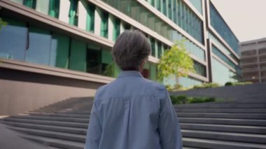 Beyaz saçlı yaşlı iş kadını merdivenlerden çıkıp modern ofis binasına gidiyor tanınmayan iş kadını şehrin başarılı feminizminde merdivenlere tırmanıyor.